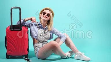 漂亮的女孩带着红色的手提箱微笑着看着相机。 女孩要去旅行了。